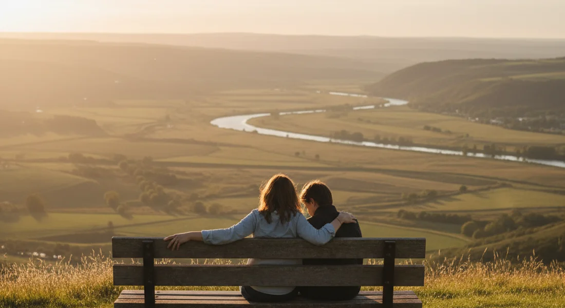 Two people sitting together on a bench overlooking a quiet landscape